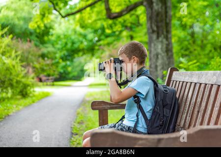 Tourist with a camera. A boy with a camera takes pictures of nature in the park. A young photographer sits on a park bench and takes pictures of Stock Photo