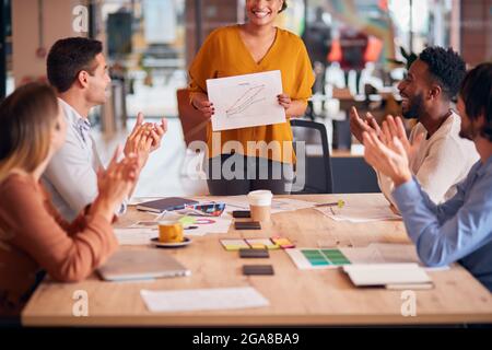 Colleagues Applauding As Businesswoman Gives Presentation In Modern Open Plan Office Stock Photo