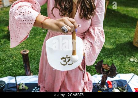 Young mexican woman on her knees playing a crystal singing bowl in holistic therapy session in Latin America Stock Photo