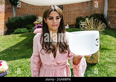 Young hispanic woman holding a crystal singing bowl in holistic therapy Stock Photo