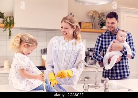 Smiling Family Having Fun In Kitchen Doing Washing Up At Sink Together Stock Photo