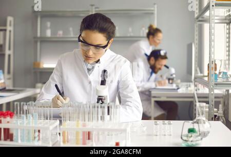 Portrait of young serious female scientist making notes sitting at lab desk Stock Photo