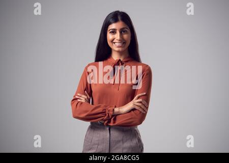 Studio Portrait Of Smiling Young Businesswoman With Folded Arms Against Plain Background Stock Photo