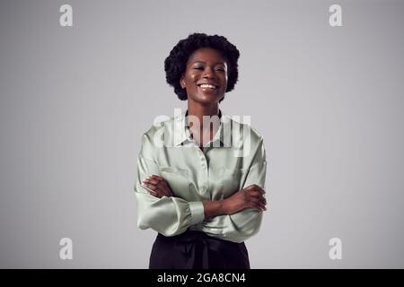 Studio Portrait Of Smiling Young Businesswoman With Folded Arms Against Plain Background Stock Photo