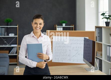Portrait of smiling young caucasian female teacher holding grade book in hand Stock Photo