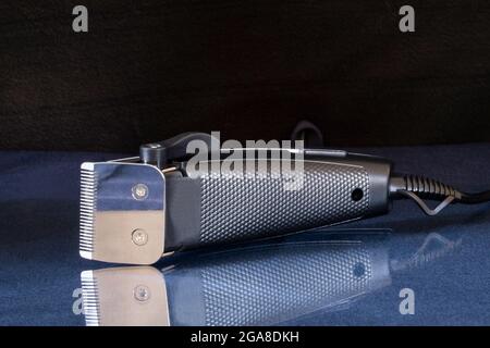 An electric razor for cutting hair is lying on a glass table. Equipment and tools on a black background Stock Photo