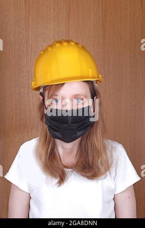 Young female worker wearing protective helmet and medical face mask working in construction industry Stock Photo