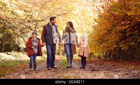 Family With Mature Parents And Two Children Holding Hands Walking Along Track In Autumn Countryside Stock Photo