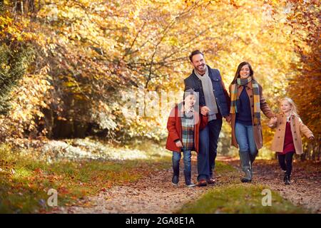 Family With Mature Parents And Two Children Holding Hands Walking Along Track In Autumn Countryside Stock Photo