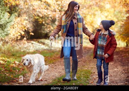 Mother And Son Take Pet Golden Retriever Dog For Walk On Track In Autumn Countryside Holding Hands