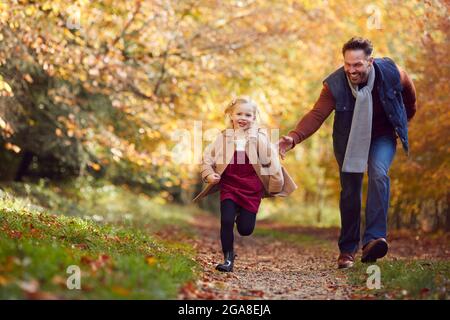 Father And Daughter On Family Walk Along Track In Autumn Countryside With Girl Running Ahead Stock Photo