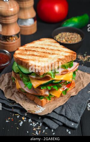 Grilled sandwich with ham, cheese and fresh vegetables on a dark background with ingredients and spices. Vertical view. Stock Photo