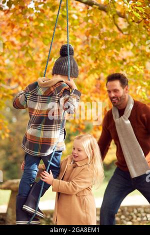 Father Pushing Children Having Fun On Rope Swing In Autumn Garden Stock Photo