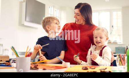 Mother With Children At Home Doing Craft And Making Picture From Leaves In Kitchen Stock Photo