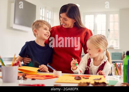 Mother With Children At Home Doing Craft And Making Picture From Leaves In Kitchen Stock Photo