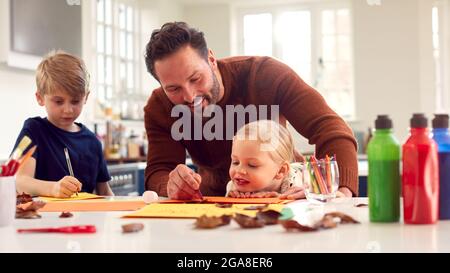 Father With Children At Home Doing Craft And Making Picture From Leaves In Kitchen Stock Photo