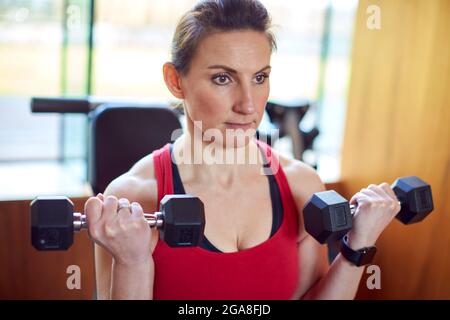 Mature Woman Exercising In Home Gym Lifting Hand Weights Stock Photo