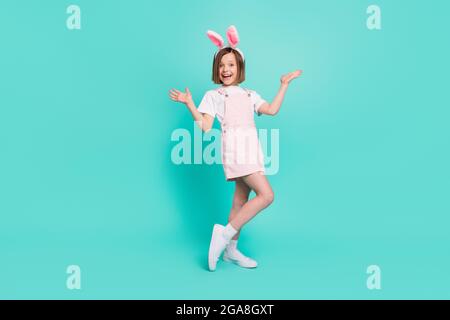 Photo of funky impressed school girl wear pink overall bunny ears smiling rising arms isolated teal color background Stock Photo