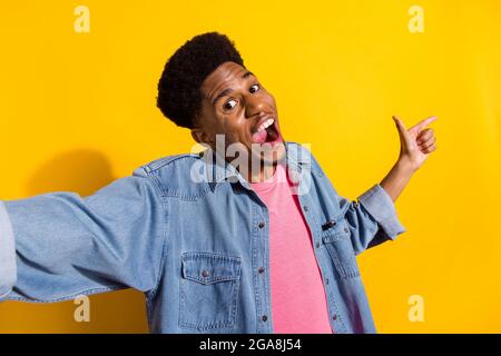 Photo of pretty impressed dark skin guy dressed denim recording video pointing finger empty space isolated yellow color background Stock Photo