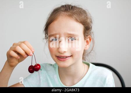 Happy surprised little girl holds cherries in hand. Healthy eating concept, healthy sweets Stock Photo