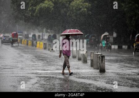 A man seen holding an umbrella while walking along an empty and deserted road during a rainy day amid the covid-19 lockdown.The country went into a strict lockdown and Heavy monsoon downpour caused extreme water logging in most areas of Dhaka city. Roads were submerged making travel slow and dangerous. Stock Photo