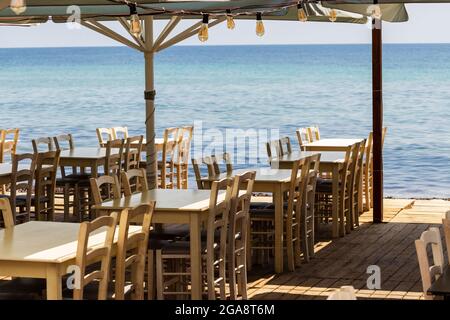 Chairs and tables of restaurants on the beach ready for guests overlooking the open sea Stock Photo