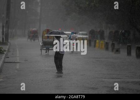 A man seen holding an umbrella while walking on an empty and deserted road during a rainy day amid the covid-19 lockdown.The country went into a strict lockdown and Heavy monsoon downpour caused extreme water logging in most areas of Dhaka city. Roads were submerged making travel slow and dangerous. Stock Photo