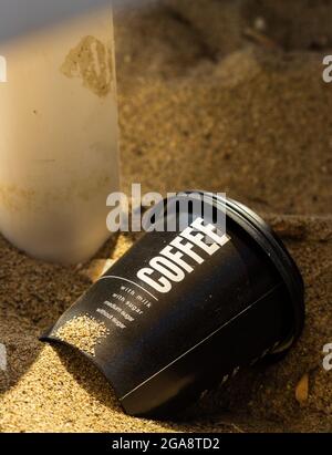Discarded black plastic disposable coffee cup on the sand Stock Photo