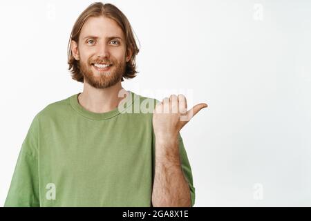 Portrait of handsome blond man smiling happy, pointing finger right, showing advertisement, promo banner aside, standing in casual green t-shirt Stock Photo