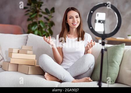 Photo portrait girl smiling doing wideo blog sitting on sofa near carton boxes Stock Photo