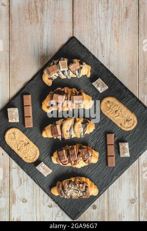 Top view on baked sweet croissants on the black plate with chocolate biscuit and cream on the table Stock Photo