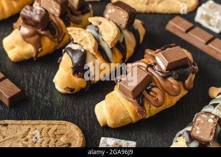 Close up on homemade baked sweet croissants on the black plate with chocolate biscuit and cream on the table Stock Photo