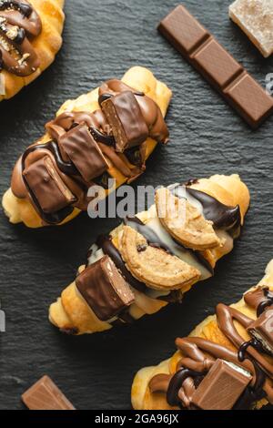 Close up on homemade baked sweet croissants on the black plate with chocolate biscuit and cream on the table Stock Photo