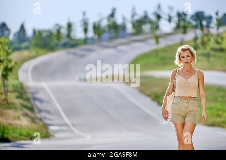 Slim white female with blonde hair goes on road. Stock Photo