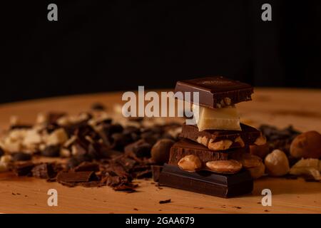 Ounces of chocolate forming a tower in the right foreground, some filled with almonds and hazelnuts. In the background a mixture of chocolate in small Stock Photo