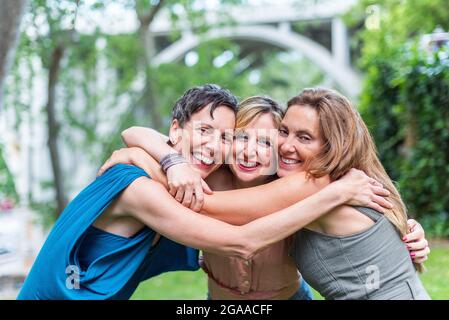 Three happy mature female friends hugging together and looking to camera Stock Photo