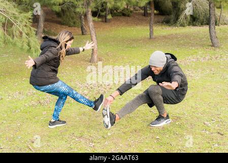Fitness couple in warm clothes standing on one leg and stretching the other Stock Photo
