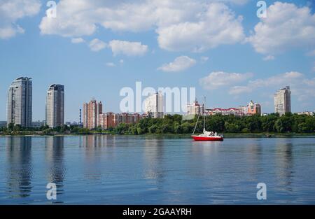 Panorama of Kyiv city scape of Dnipro River. Modern residential building, yacht and park with urban street landscape by the river. Stock Photo