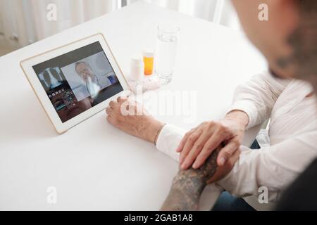Close-up of family of two sitting at the table and talking to doctor online using digital tablet Stock Photo