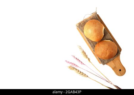 two buns on a cutting board and ears of wheat isolated on white background flat lay. Image contains copy space Stock Photo