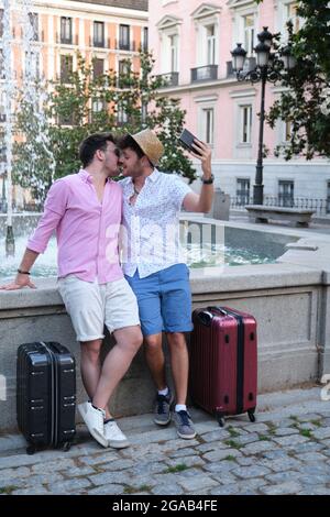 Gay tourist couple kissing and taking a selfie at fountain in a city square. Stock Photo