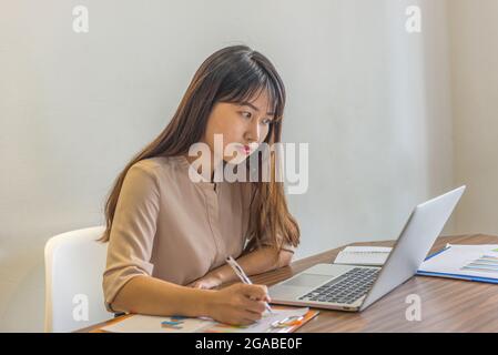 Young freelancer writing notes and working on laptop at home Stock Photo