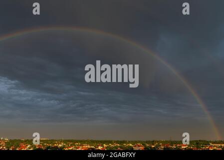 Rainbow over stormy sky. Double rainbow over city with a dramatic sky in the background. Gloomy dark sky in the background during a rainy day. Beautif Stock Photo