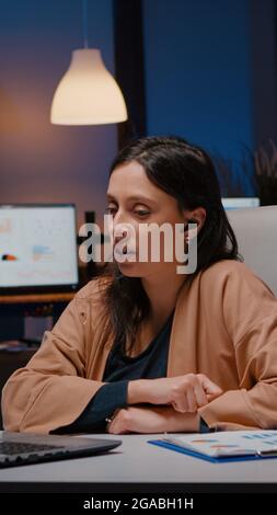 Businesswoman with headphones discussing marketing statistics planning business strategy. Entrepreneur woman talking with her collegues during online videocall conference company meeting in evening Stock Photo