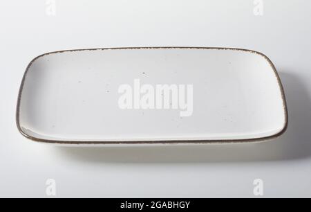 From above ceramic rectangle shaped plate with white enamel and black rim placed on gray background Stock Photo