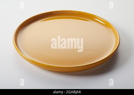 High angle of round ceramic plate with shiny orange enamel placed on gray background Stock Photo