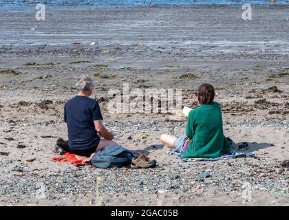 older couple sitting on a stony beach, togetherness, couple at the seaside, married couple on the beach, middle-aged couple at the coast together. Stock Photo