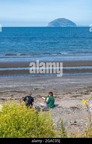 man and woman sitting on sandy beach, couple sitting on scottish sandy beach, couple enjoying ailsa craig views from girvan beach in ayrshire, seaside Stock Photo