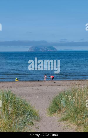 ailsa craig island off of the ayrshire coast at girvan with a family playing on girvan beach in the foreground. sandy beach at girvan ayshire. Stock Photo