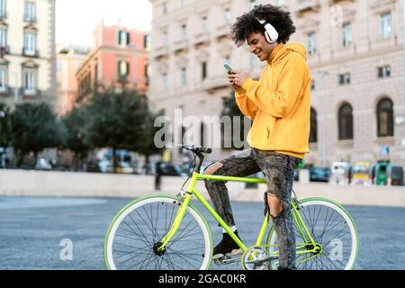 Happy African man using mobile smartphone outdoor - Young guy having fun riding with bike in the city Stock Photo